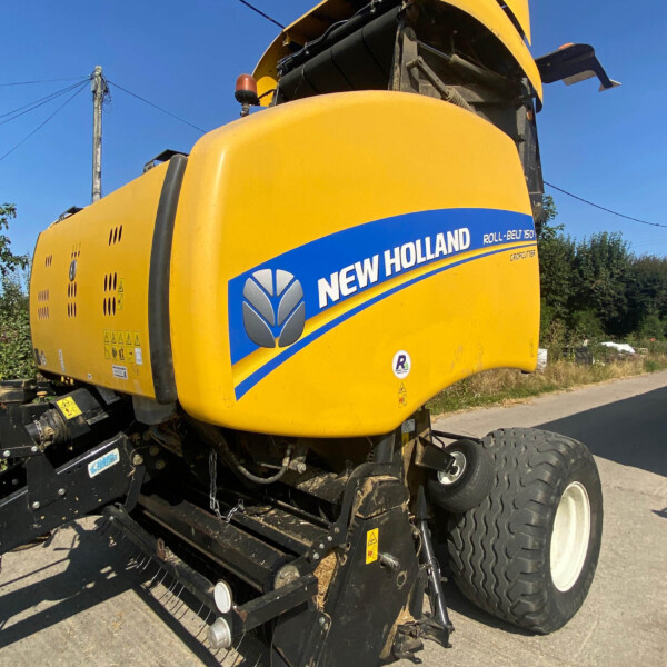 Yellow New Holland Roll-Belt 150 agricultural harvester viewed from the side, logo and blue stripe visible on the body behind the cab window area.