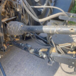 Close-up of dusty hydraulic hoses and metal framework on heavy farm equipment, with a yellow caution label nearby
