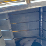 Close-up of industrial machinery showing a hydraulic piston/connector and rusted metal beams above blue-painted panels.