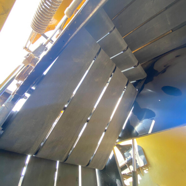 Industrial machine interior showing parallel black metal slats and a coiled hose with a yellow frame nearby