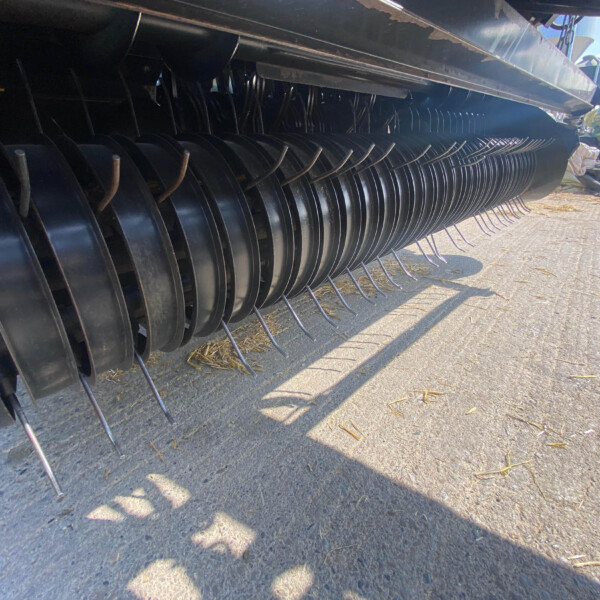 Close-up of a combine harvester header with curved metal tines along a black housing.