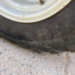 Close-up of a worn tire sidewall showing embossed size and serial markings, with part of a white wheel rim above.