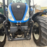 Front view of a blue tractor with a large grille and oversized front tires; there is another blue tractor in the background at a dealership yard.