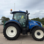 Close-up of a blue New Holland tractor front with large white wheels, orange beacon on top, parked on a lot.