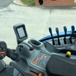 Inside the tractor cab showing a joystick, steering, and a colorful array of function buttons on the dashboard.