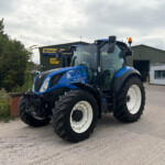 Blue New Holland tractor parked outside an agricultural service building with a cloudy sky above.