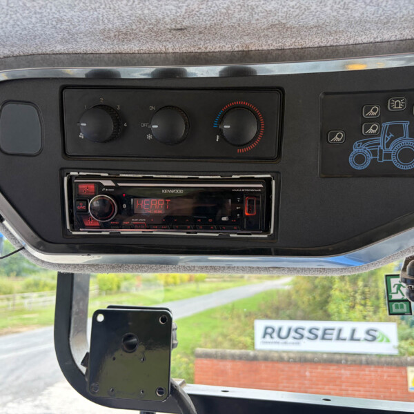 DashboardControls: three climate knobs and a Kenwood stereo, with a blue tractor graphic on the right panel and a 'RUSSELLS' sign visible outside the window.