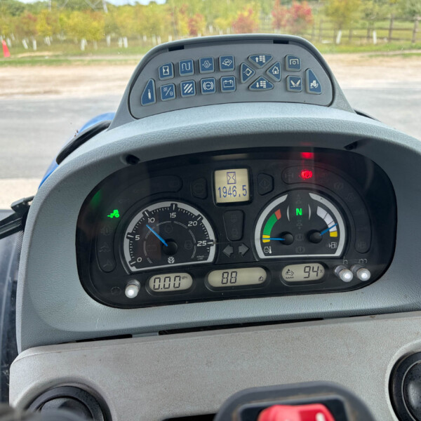 Close-up of a tractor dashboard with a row of blue control icons and digital readouts, outdoors in the background.