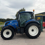 Close-up of a blue New Holland tractor at a dealership yard, showing large white wheels and front tire treads.