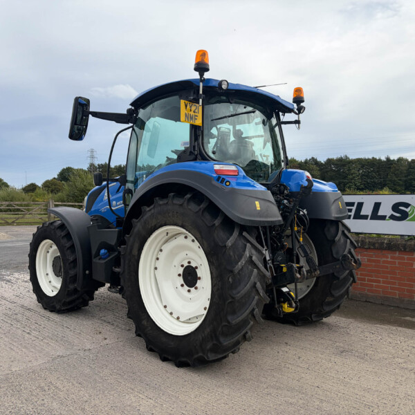 Front-left view of a blue agricultural tractor with large white wheels and orange beacon lights in a parking yard outdoors on a cloudy day