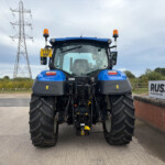 Rear view of a large blue tractor with oversized tires, two orange beacon lights, and a yellow YY21 NMF plate beside a brick wall and power lines in the background.