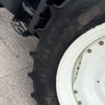 Close-up of a heavy tire and white wheel, showing tread, lug nuts, and part of the rim on a concrete surface