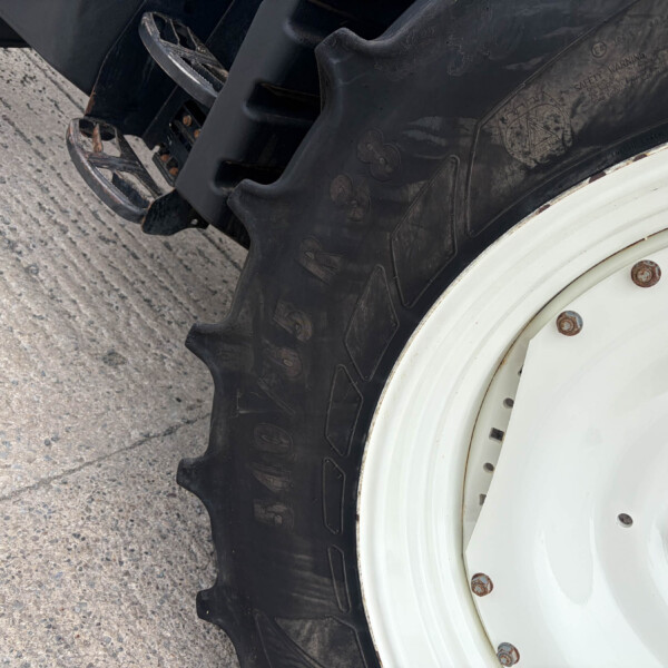 Close-up of a heavy tire and white wheel, showing tread, lug nuts, and part of the rim on a concrete surface