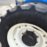 Close-up of a large tractor tire with deep tread and a white rim, blue tractor body visible in the background.
