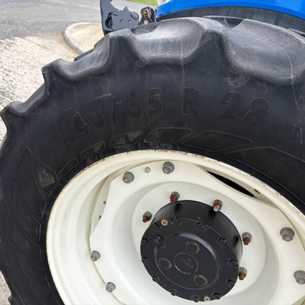 Close-up of a large tractor tire with deep tread and a white rim, blue tractor body visible in the background.
