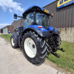Blue agricultural tractor with large white wheels parked outside a metal-sided building on a sunny day.