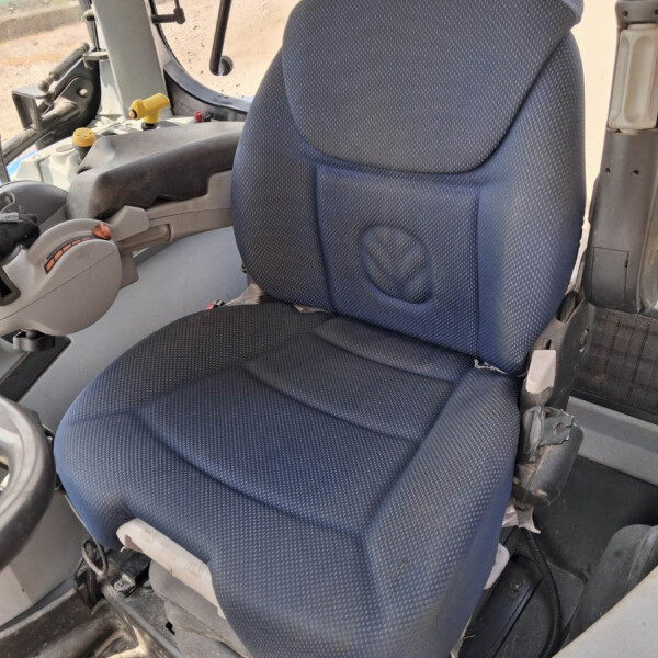 Blue fabric driver's seat in a dusty construction vehicle cab, with controls and steering wheel nearby.
