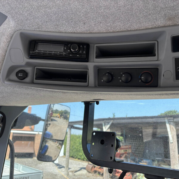 Interior of a tractor cab with radio, climate controls, and a windshield showing a construction site outside