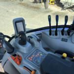 Interior of a heavy machinery cab with five vertical blue-lever controls and a right-side display panel behind the steering area