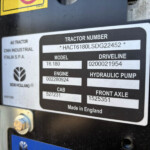 Close-up of a tractor identification plate with the label 'TRACTOR NUMBER' and serial/model numbers, including 'Made in England' text on a dark metal surface.