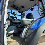 Inside view of a blue tractor cab: driver’s seat, steering wheel, and control panel visible through the open door.