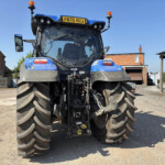 Front view of a blue agricultural tractor with oversized rear tires, muddy wheels, and orange warning lights in a rural driveway setting.