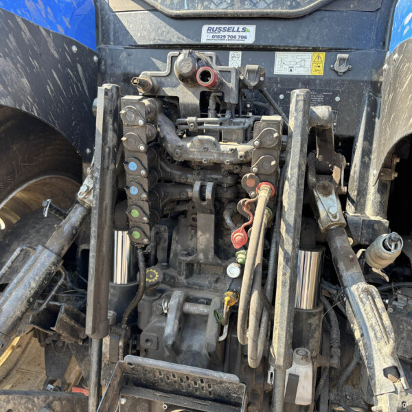 Close-up of a tractor's front hydraulic hitch with hoses, valves, and red caps, muddy from field use