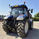 Front view of a large blue tractor with oversized tires in a gravel lot on a sunny day.