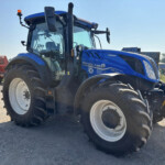 Blue New Holland tractor in a rural equipment yard, close-up front view on a gravel surface