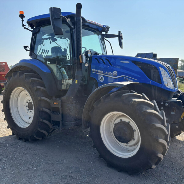 Blue New Holland tractor in a rural equipment yard, close-up front view on a gravel surface