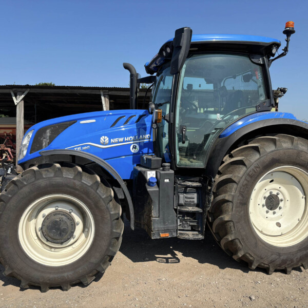 Blue New Holland tractor viewed from the side, showing large front and rear tires and the cab under a clear blue sky.
