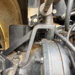 Close-up of dusty agricultural machinery hydraulics with hoses, bolts, and metal brackets