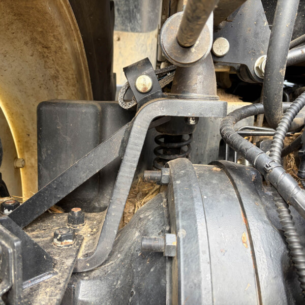 Close-up of dusty agricultural machinery hydraulics with hoses, bolts, and metal brackets