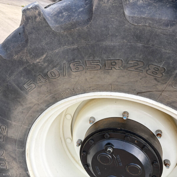 Close-up of a large off-road tractor tire showing deep treads and a white rim with bolts.