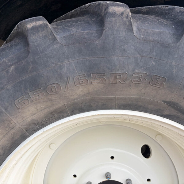 Close-up of a large tractor tire with a white rim and lug nuts; visible dirt and scuffs on the tread. Tire size 650/65R38 partially visible.
