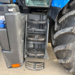 Close-up of a farm tractor step ladder between the large rear tire and a black maintenance panel on a blue tractor surface.