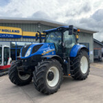 Blue New Holland tractor parked outside a New Holland Agriculture dealership building with a yellow-blue sign above the entrance.