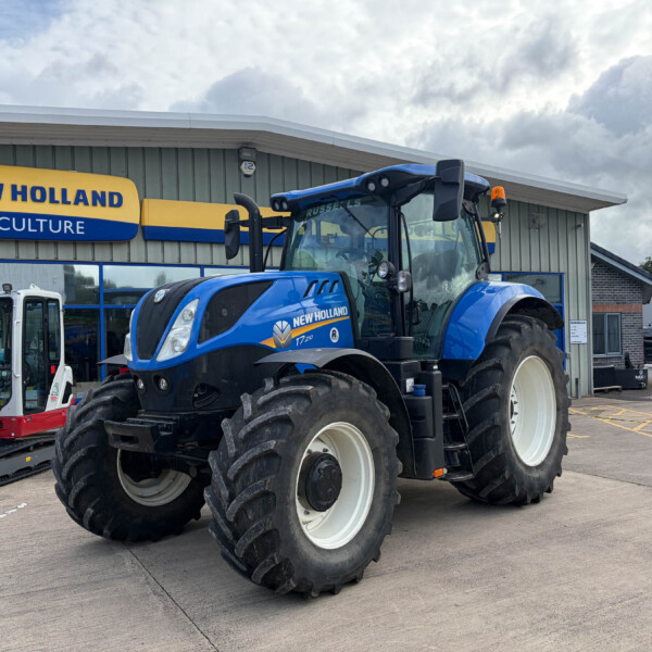 Blue New Holland tractor parked outside a New Holland Agriculture dealership building with a yellow-blue sign above the entrance.