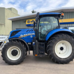 Blue New Holland tractor parked in a lot in front of a farm equipment building with yellow and blue signage