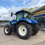 Large blue New Holland tractor with oversized tires parked in front of a New Holland Agriculture building.