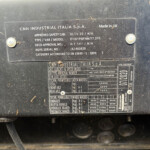 Close-up of a dusty metal data plate on heavy equipment showing CNH INDUSTRIAL ITALIA S.p.A. and model/serial details for identification, including 'Made in UK'.