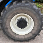 Close-up of a large tractor tire with deep tread and a white rim, blue tractor body visible in the background.