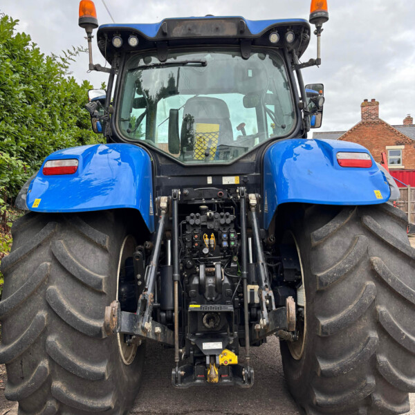 Front view of a blue tractor with oversized rear tires, orange warning lights, and a visible cabin.