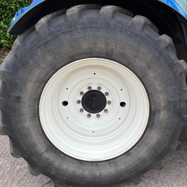 Close-up of a large tractor tire with a blue fender above and a white wheel rim visible in front