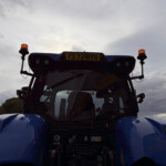 Rear view of a blue truck cab with two orange beacon lights on stalks and a yellow license plate reading FE72 BYU against a cloudy sky.