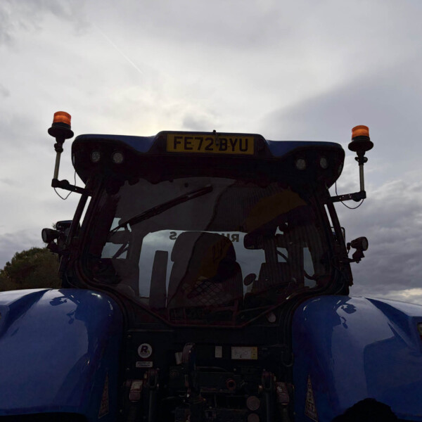 Rear view of a blue truck cab with two orange beacon lights on stalks and a yellow license plate reading FE72 BYU against a cloudy sky.