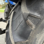 Close-up of a large tractor tire with dirt and a parking lot in the background.