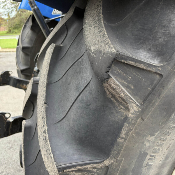 Close-up of a large tractor tire with dirt and a parking lot in the background.