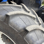 Close-up of a large muddy tractor tire with rugged tread and part of the wheel rim visible at the bottom left.