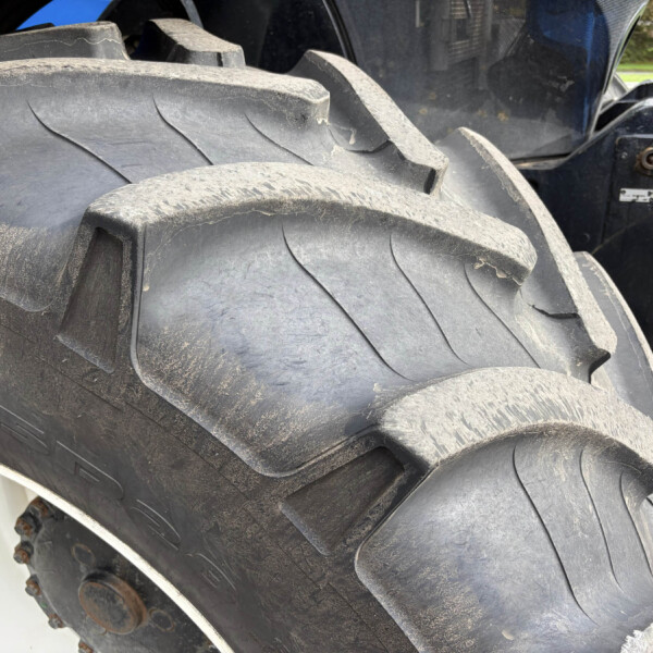 Close-up of a large muddy tractor tire with rugged tread and part of the wheel rim visible at the bottom left.